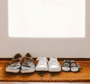 A collection of family shoes, including baby booties, on a welcoming mat by the door.